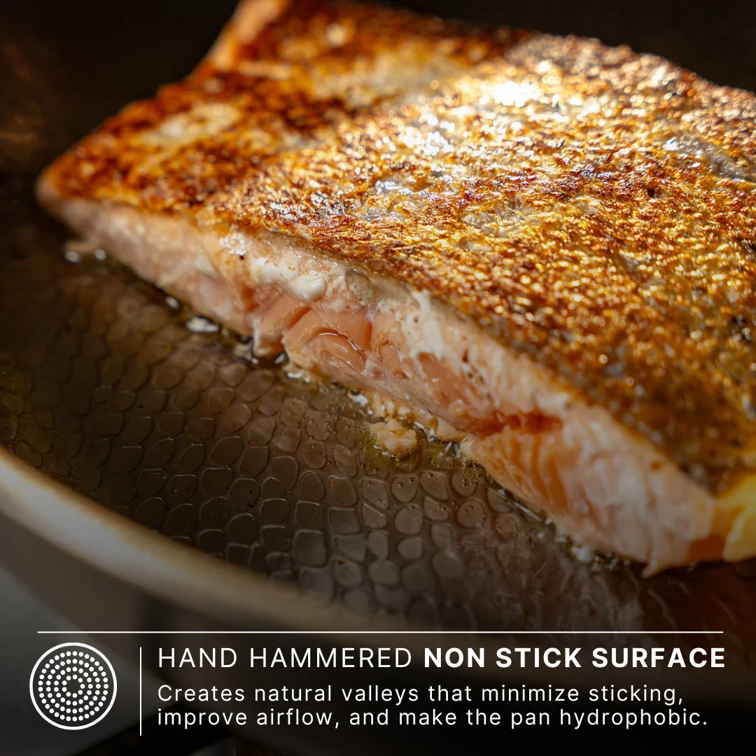 Salmon fillet searing on Siraat titanium hammered pan showing natural non-stick surface that creates valleys to minimize sticking and improve airflow