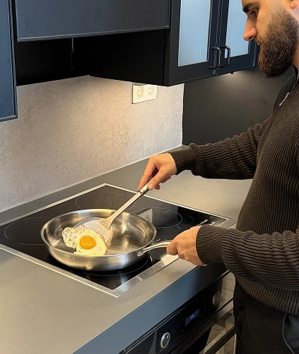 Customer cooking eggs with natural non-stick release on a Siraat titanium hammered pan on an induction cooktop