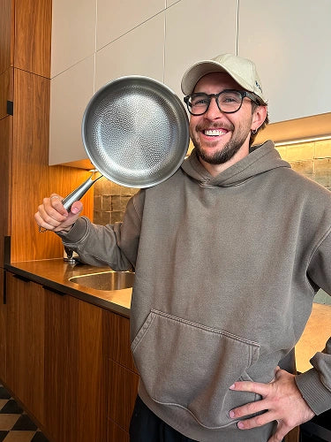 Satisfied customer holding up Siraat Titanium Hammered Pan Pro in a modern kitchen, demonstrating how lightweight the pan is