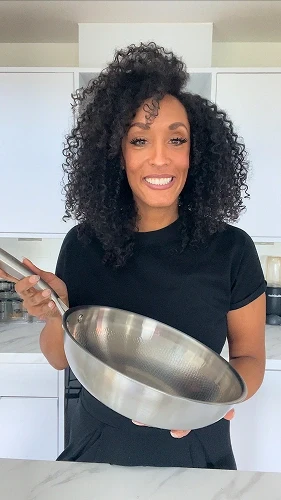 Happy customer holding Siraat Titanium Hammered Wok Pan in a white kitchen, showcasing the lightweight design